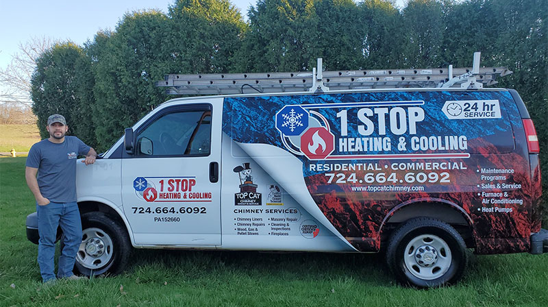One Stop Heating and Cooling Van with Logo.  Ladders on the top with tech standing beside van.  A line of trees and blue sky in the background.
