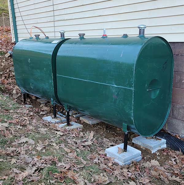 Two green heating oil tanks on side of home standing on concrete slabs.
