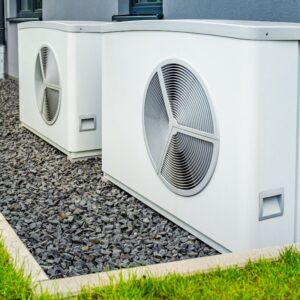 two white heat pumps sitting on rocks outside a building