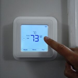 a person adjusting a smart thermostat that's reading 73 degrees